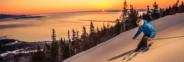 Photo d'un skieur descendant une piste de ski devant un coucher de soleil